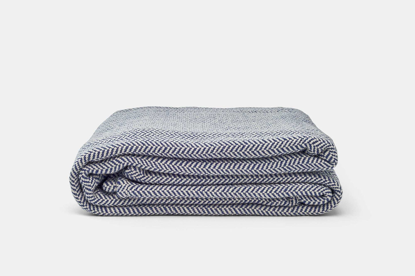 Folded blue and white herringbone weave cotton blanket on a white background