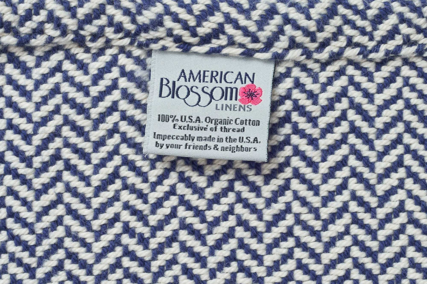 Close-up of blue and white herringbone weave cotton blanket with American Blossom Linens label