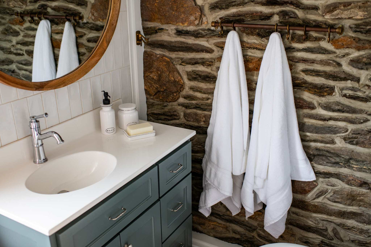 luxurious white bath towels hanging on rustic stone wall near blue bathroom vanity with sink and mirror