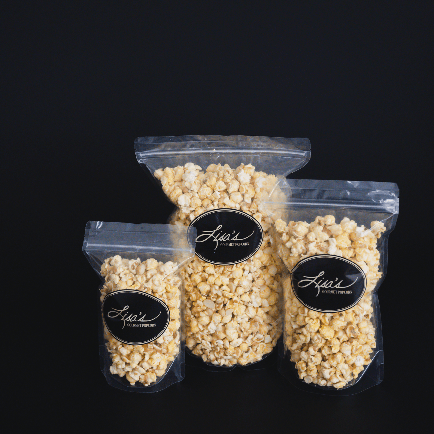 Three resealable bags of Coconut + Macadamia Nut Popcorn with candied coconut and macadamia nuts against a black background
