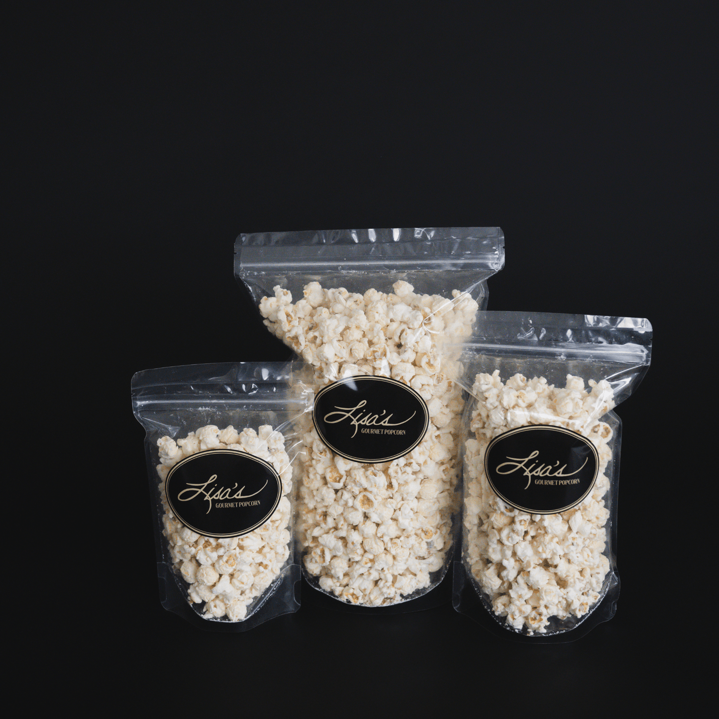 Three resealable bags of gourmet white chocolate popcorn in different sizes against a black background
