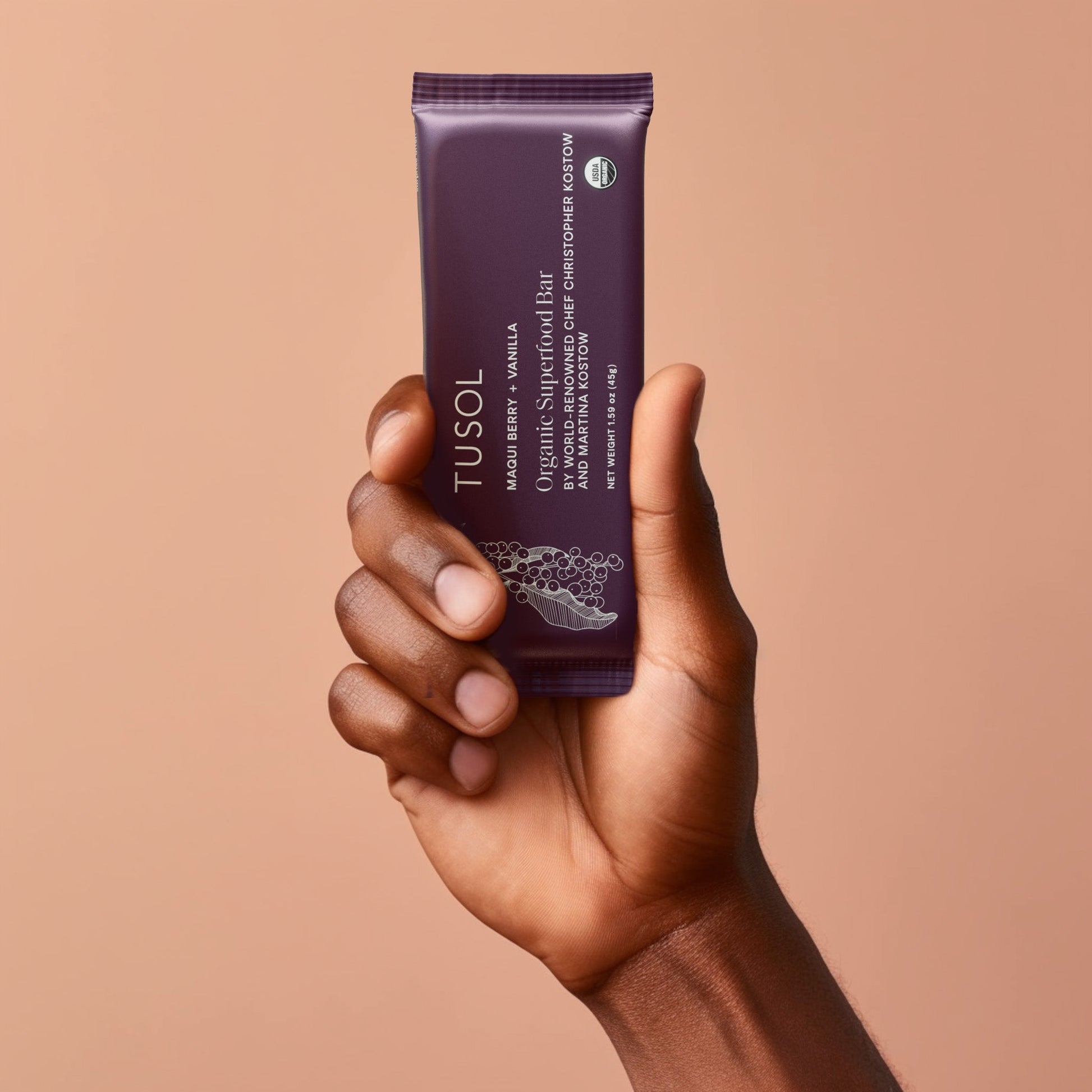 Hand holding TUSOL Wellness Essentials Starter Kit organic maqui berry vanilla protein bar package