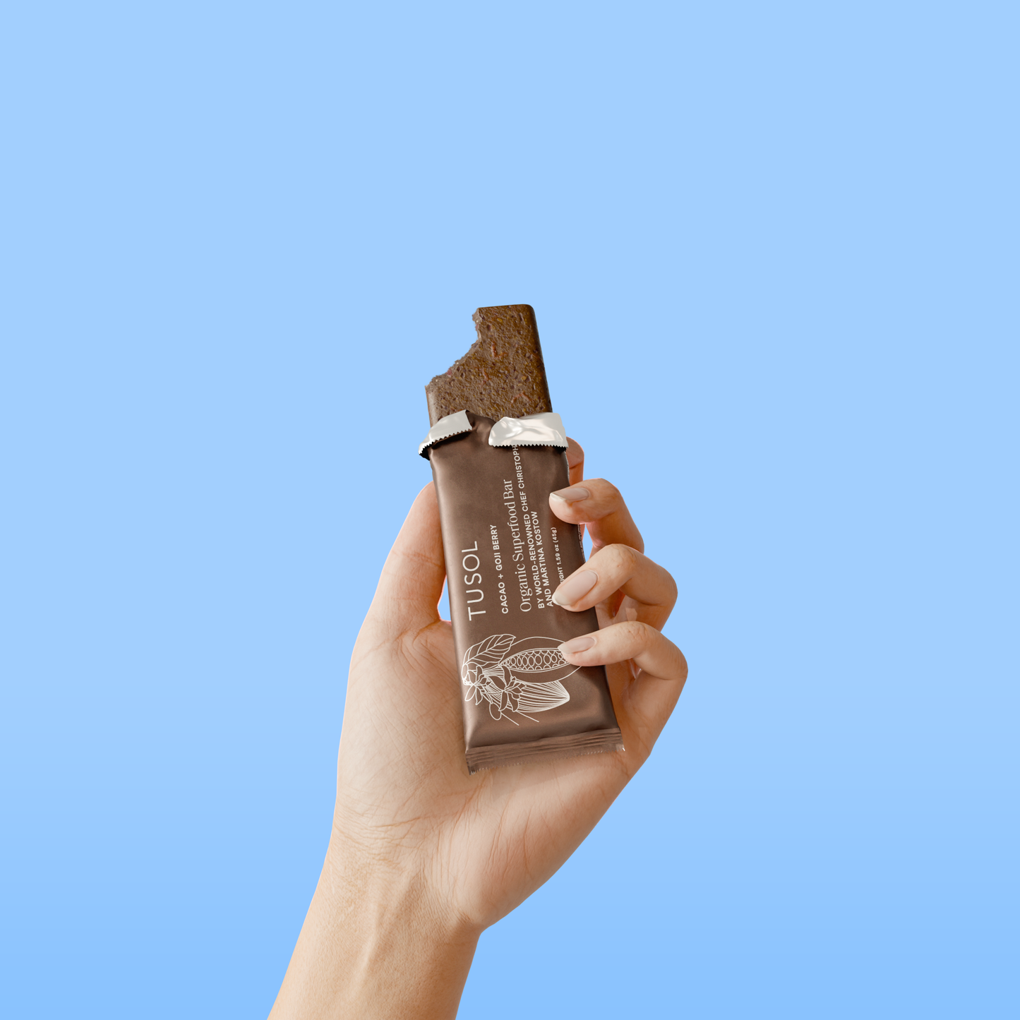 Hand holding bitten TUSOL Wellness Essentials Starter Kit organic protein bar against blue background