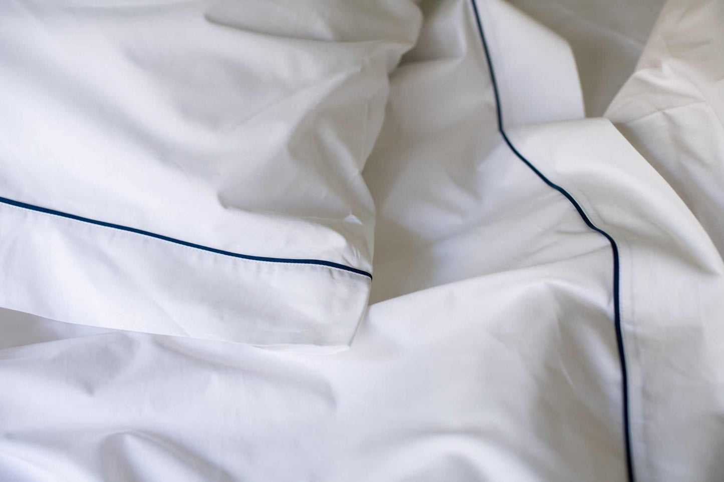 White cotton bed sheet set with blue piping design on pillowcases and edges