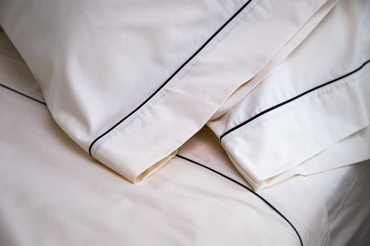 Close-up of white cotton bed sheets and pillowcases with dark piping design