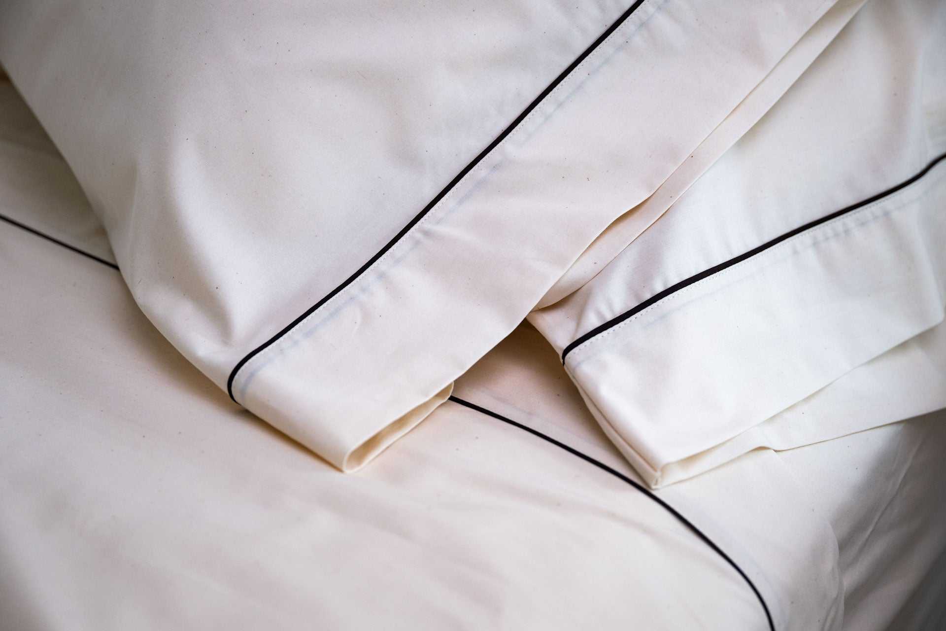 Close-up of white cotton bed sheets and pillowcases with dark piping design