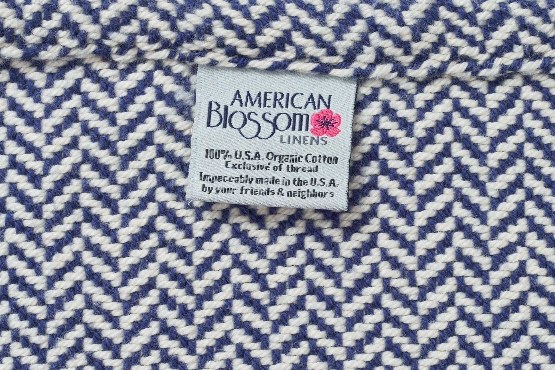 Close-up of blue and white herringbone weave cotton blanket with American Blossom Linens label