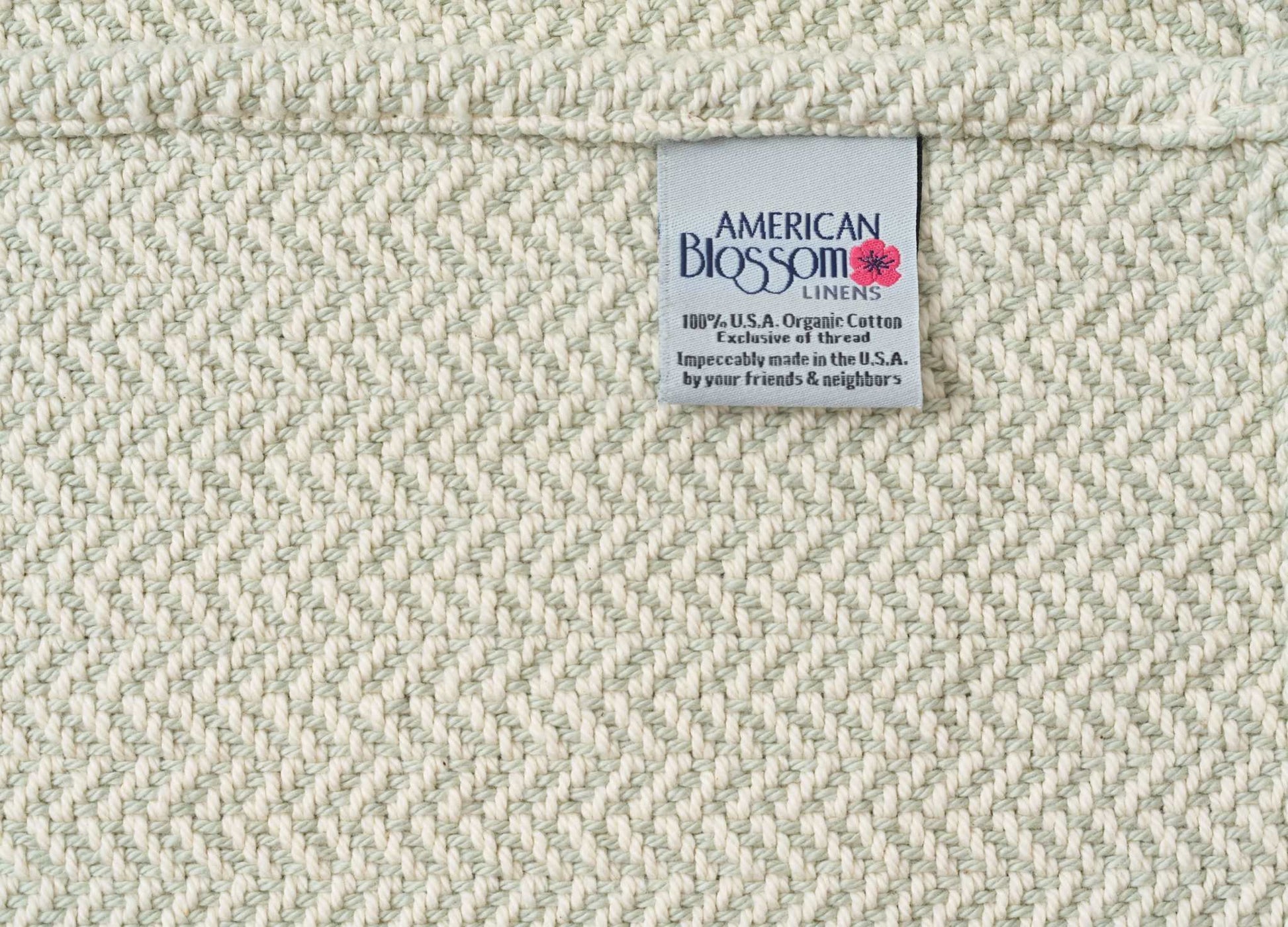 Close-up of cream-colored herringbone weave cotton blanket with American Blossom Linens tag