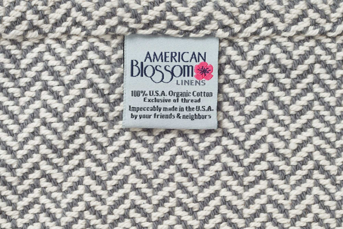 Herringbone weave cotton blanket with American Blossom Linens label showing 100% organic cotton made in the USA