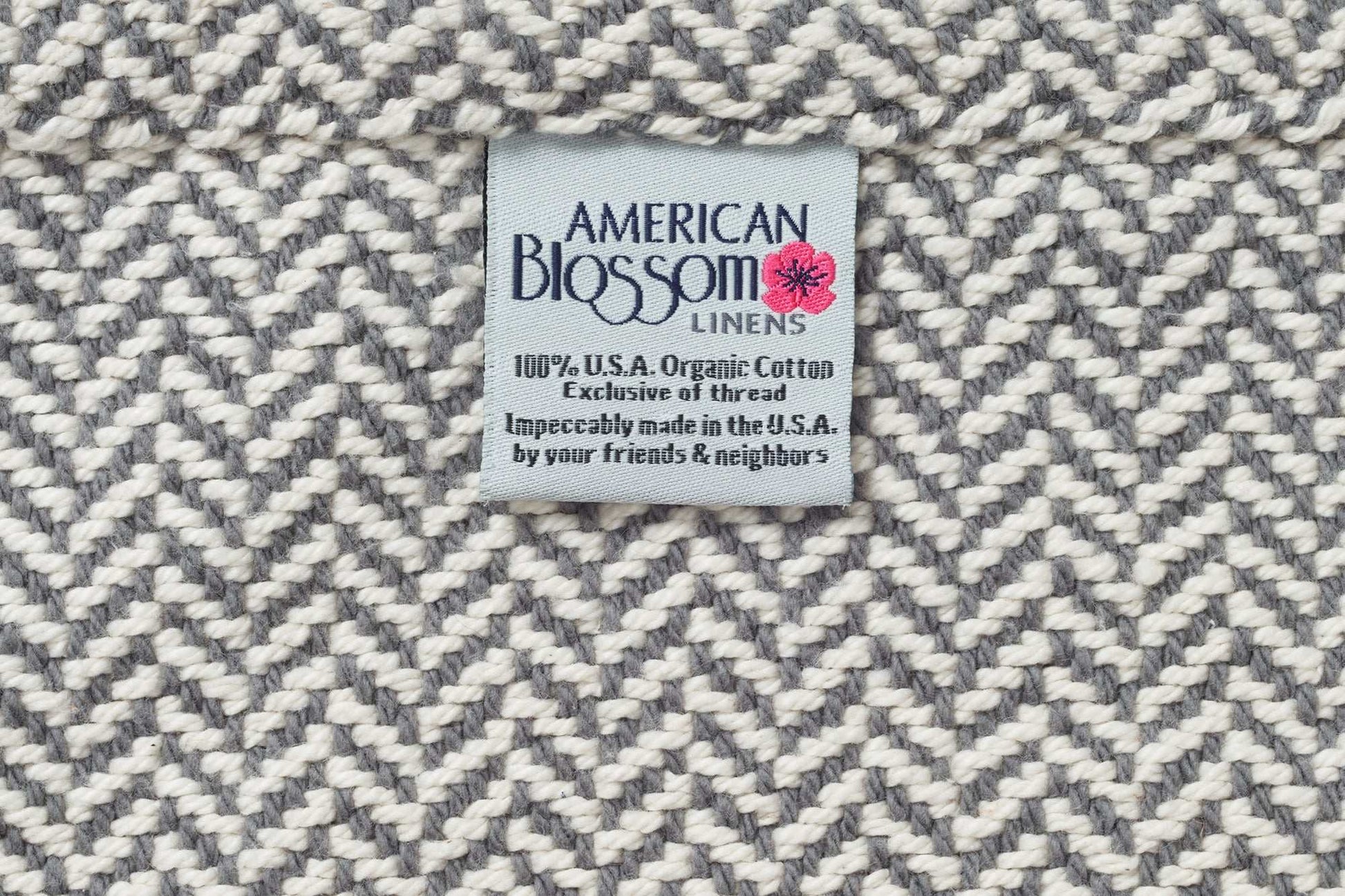 Herringbone weave cotton blanket with American Blossom Linens label showing 100% organic cotton made in the USA