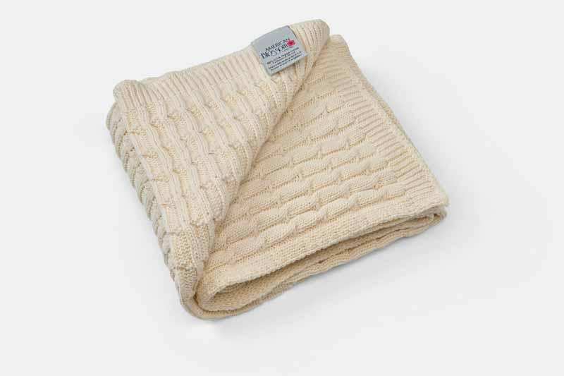 Cream-colored cotton knitted baby blanket with textured pattern folded on white background