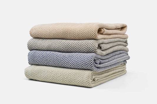Stack of folded herringbone weave cotton blankets in beige, gray, blue, and cream colors