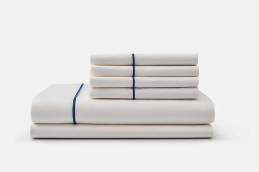 White cotton bed sheet set with blue piping design stacked neatly