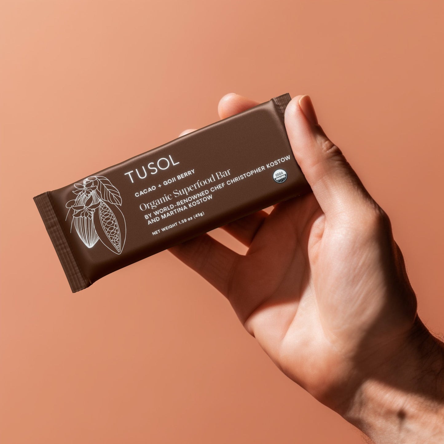 Hand holding TUSOL Cacao + Goji Berry organic protein bar with clean, organic ingredients.