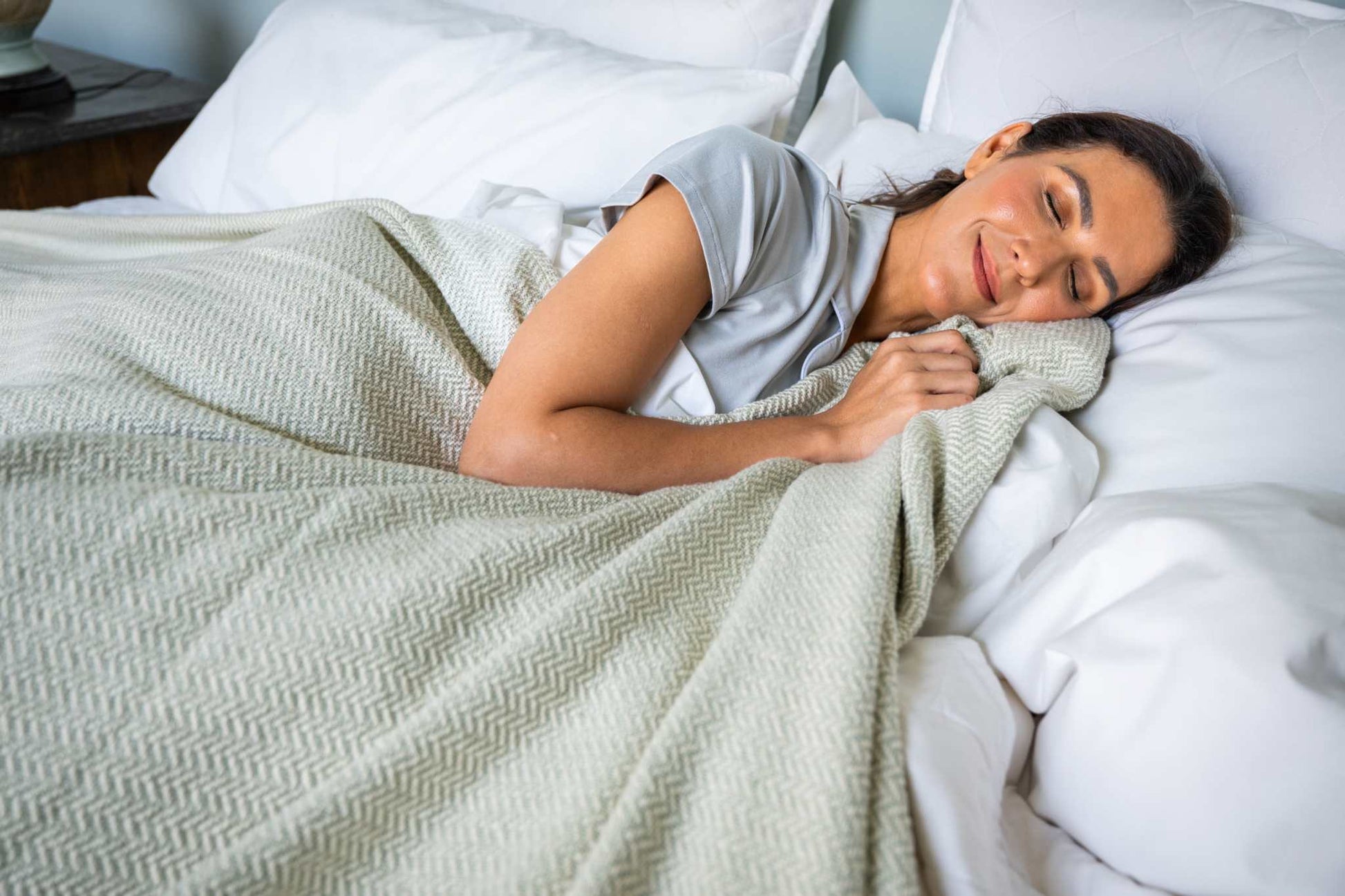 Woman sleeping comfortably wrapped in a soft herringbone weave cotton blanket on a white bed