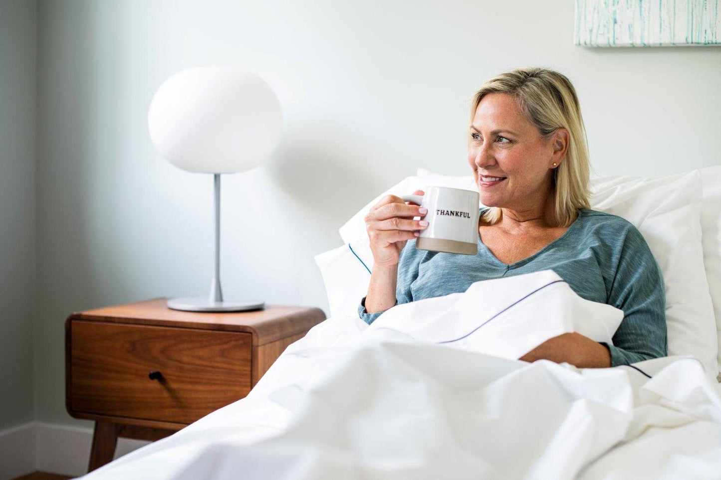 Woman relaxing in bed with white cotton piping design bed sheet set and drinking coffee