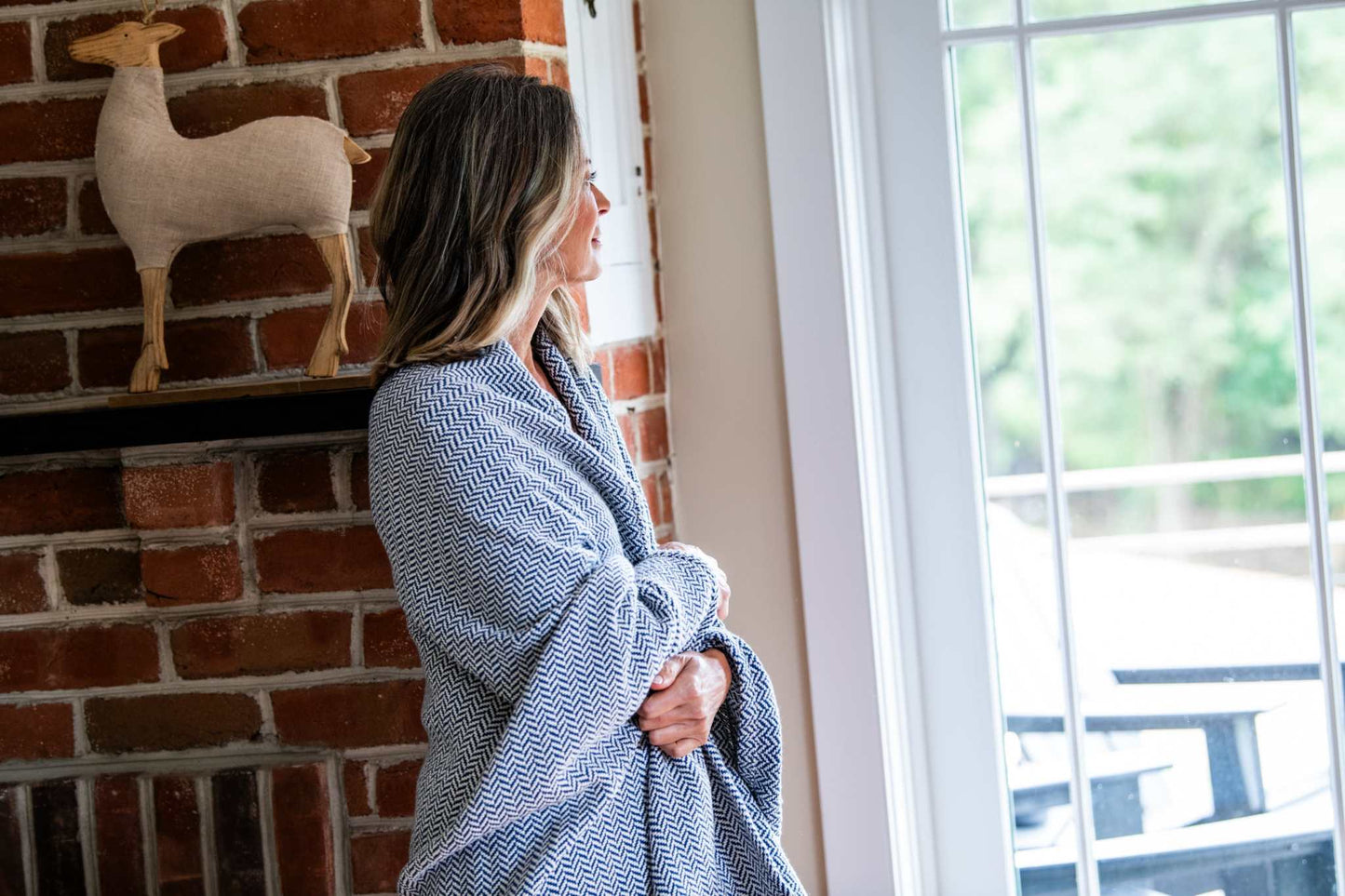 Woman wrapped in a soft herringbone weave cotton blanket standing by windowCozy herringbone weave cotton blanket wrapped around woman near window