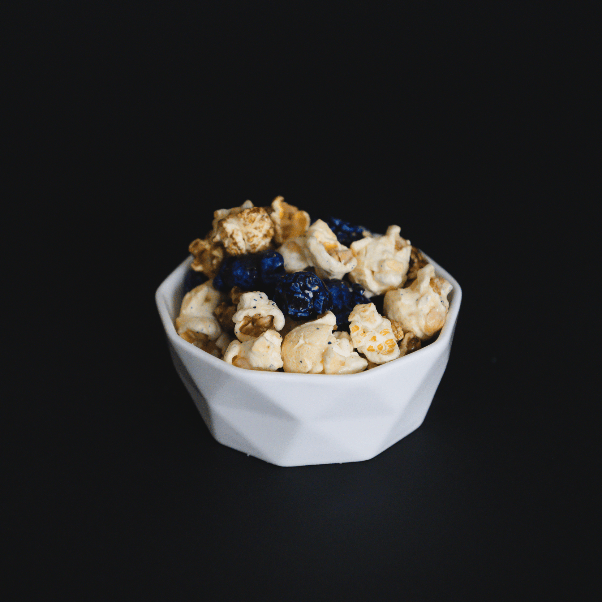 Blueberry muffin popcorn with candied sweet dough blueberry and buttery vanilla popcorn in a white bowl on black background