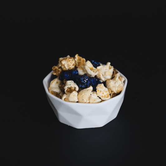Blueberry muffin popcorn with candied sweet dough blueberry and buttery vanilla popcorn in a white bowl on black background