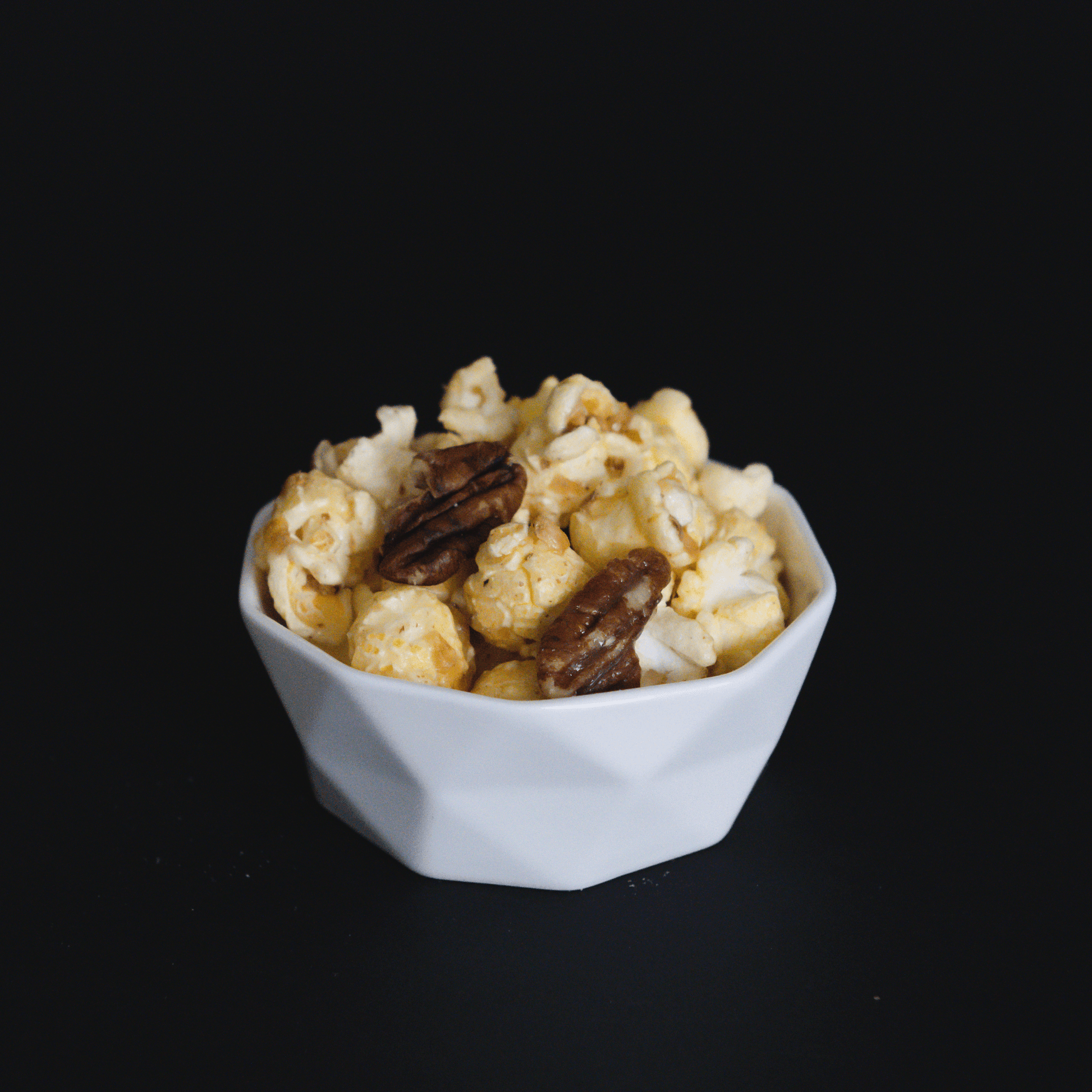 Butter pecan popcorn with crunchy pecans in a white bowl on black background