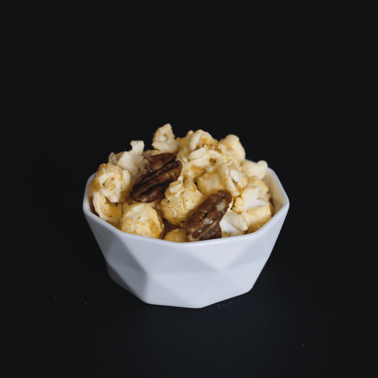 Butter pecan popcorn with crunchy pecans in a white bowl on black background