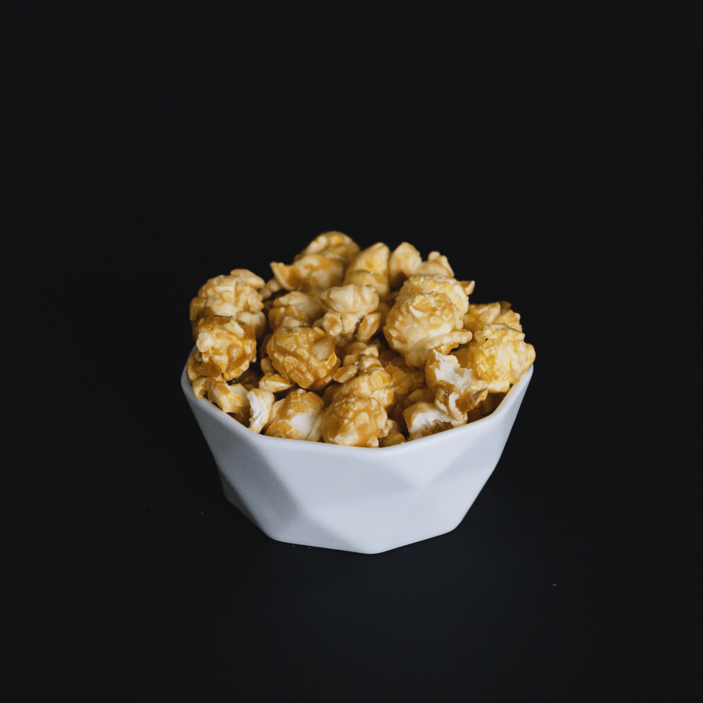White bowl filled with handcrafted caramel popcorn against black background