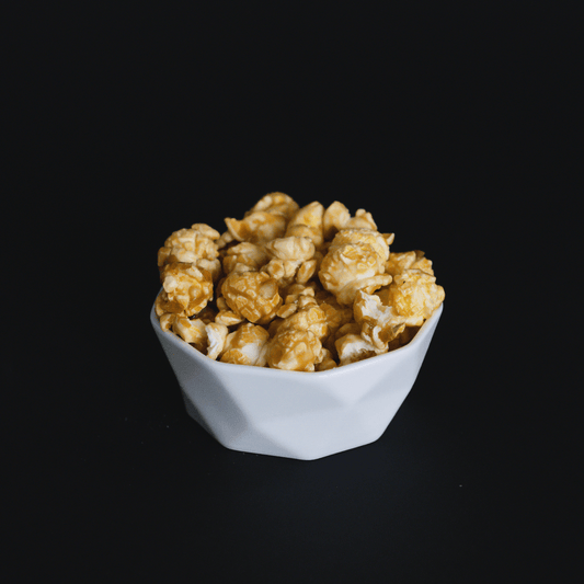 White bowl filled with handcrafted caramel popcorn against black background