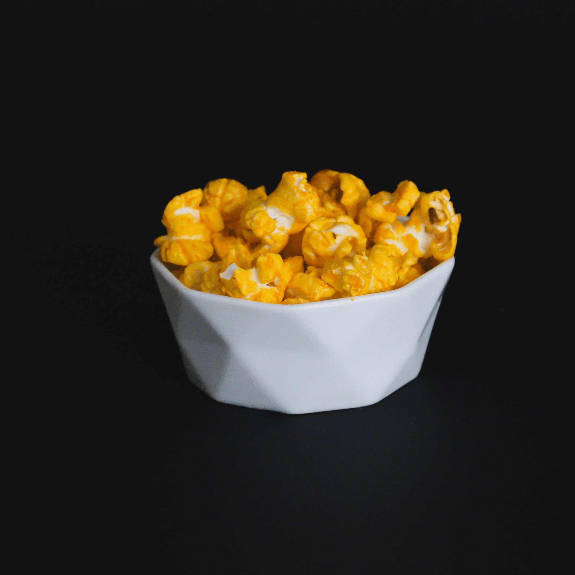 White bowl filled with crunchy cheddar cheese popcorn on black background