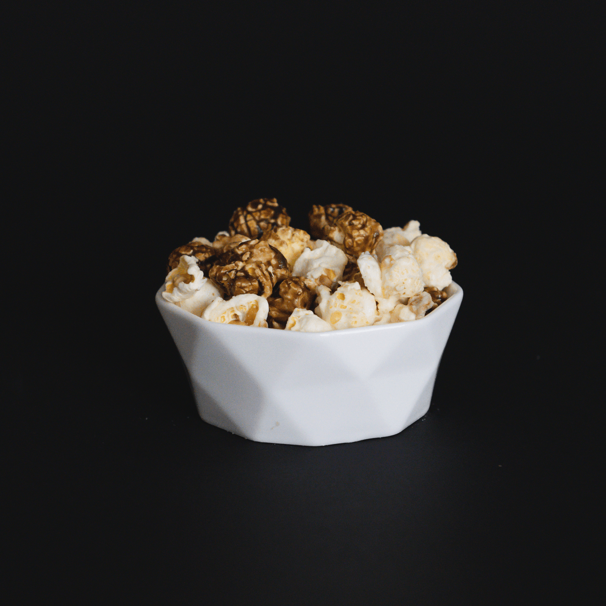 White bowl of cinnamon roll popcorn with candied cinnamon and vanilla flavors on black background