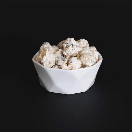 Bowl of white chocolate Cookies + Cream Popcorn with crushed chocolate sandwich cookies against black background