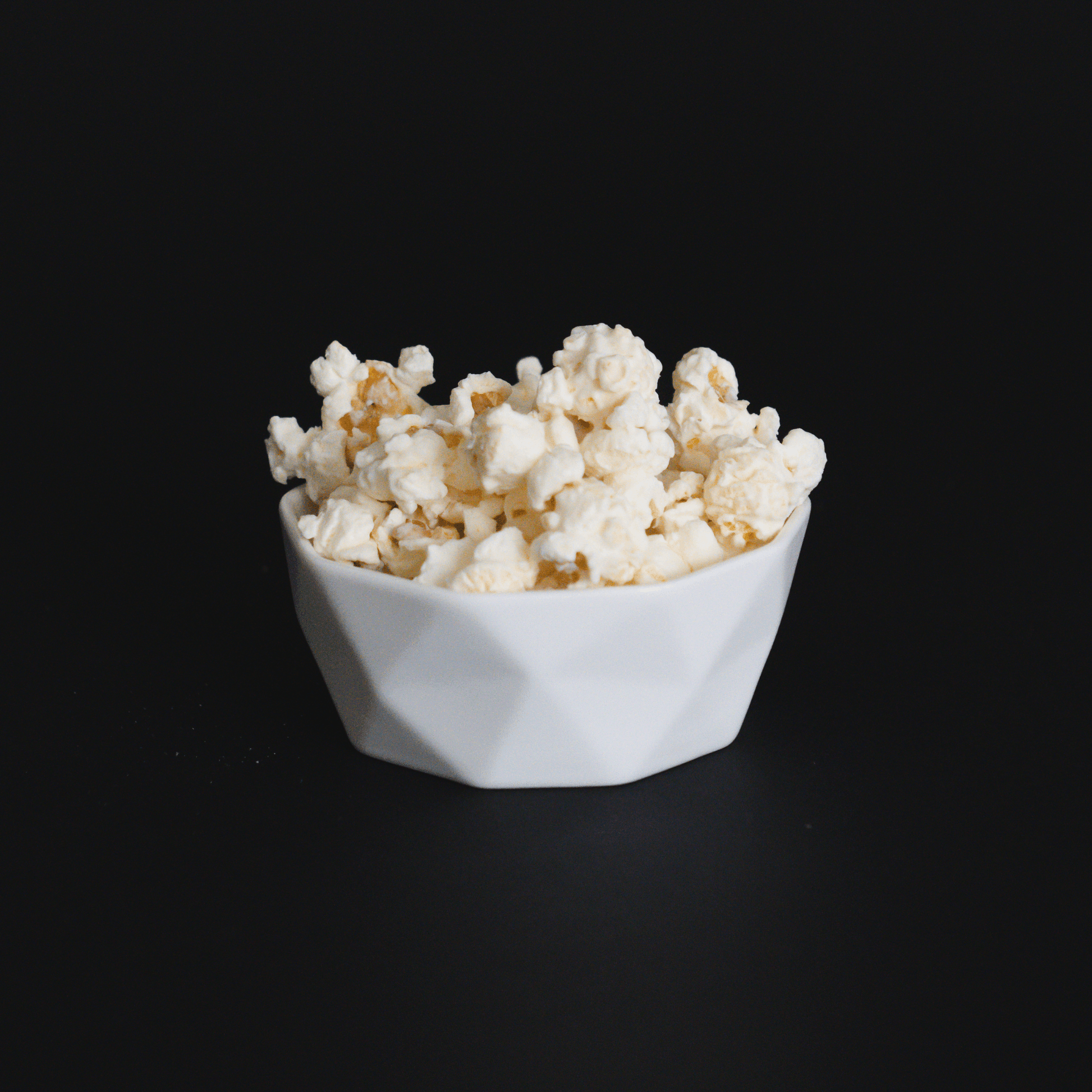 white chocolate popcorn in a white bowl on black background gourmet creamy snack